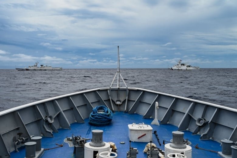 2168188450 China Coast Guard ships, in the background, are in the South China Sea, with a Philippine Coast Guard vessel in the foreground.