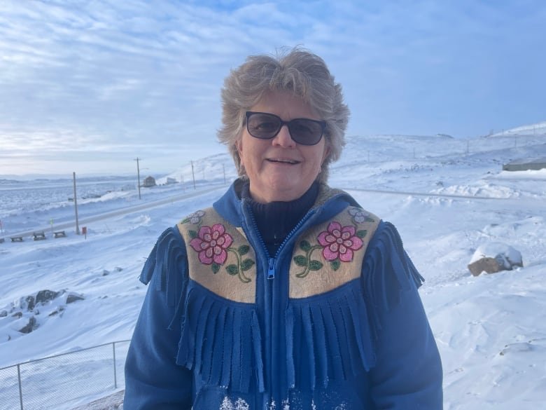 anne-crawford A woman in a blue coat stands outside with snowy, barren hills visible behind her.