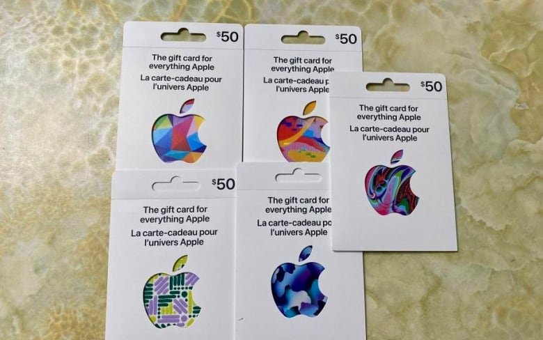 apple-gift-cards Five white $50 gift cards lay on a tiled surface. Each one has a multi-coloured Apple logo on it.