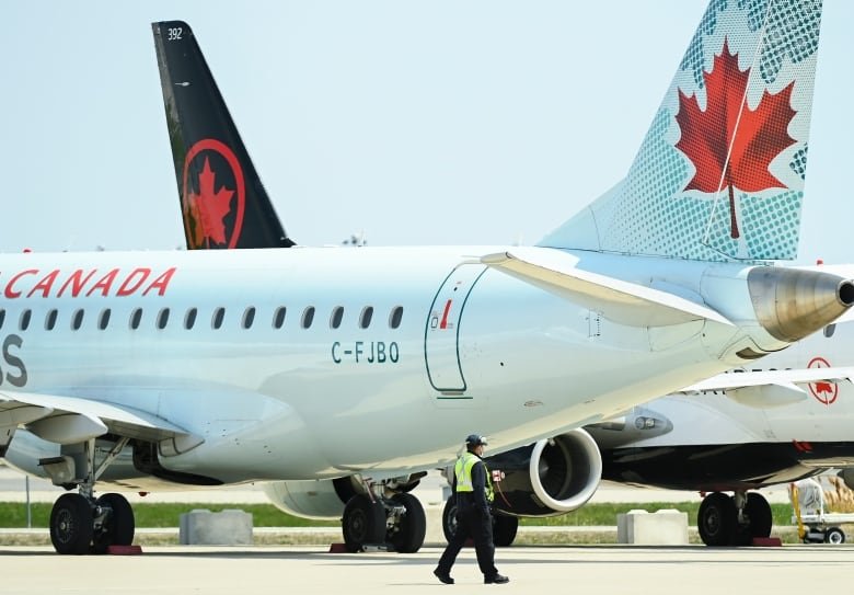 covid-cdn-airlines-20210427 Two Air Canada jetliners sit on a runaway. A man walks in front of them.