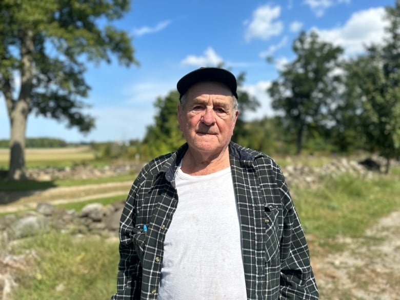 An portrait of an elderly man in a flannel shirt and cap on a farm.