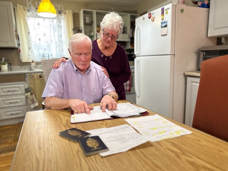 doug-and-nancy-documents An elderly white man and woman look at documents on their wooden kitchen table.