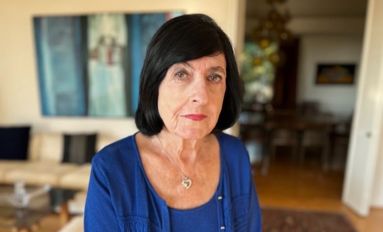 dr-vicki-bernstein An aged white woman with a black bob and blue cardigan sits in her living room