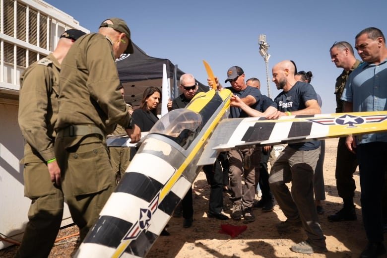 Roughly a dozen men, some in military clothing, gather around a small winged aircraft.