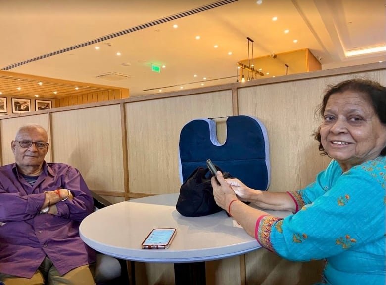 harish-at-airport A south Asian man and woman sit smiling on opposites sides of a small round table.