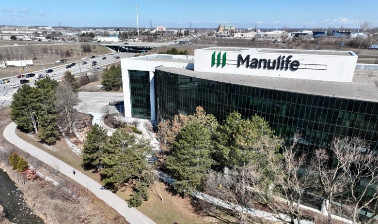 manulife-bank-waterloo A drone shot of a building with the Manulife logo on the top. It's beside a highway and behind some trees in the foreground.