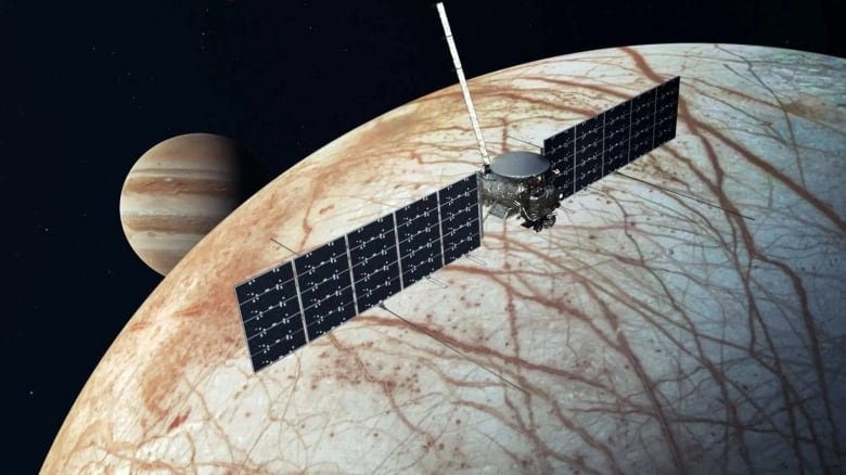 space-exploration-europa-1 A spacecraft with two long checkered panels extending out on either side of it like wings is pictured in front of a giant pale ball that takes up most of the space scenery image. This ball is unevenly striped with brown like a tiger, while in the distance, Jupiter is visible, with its even red and brown stripes.