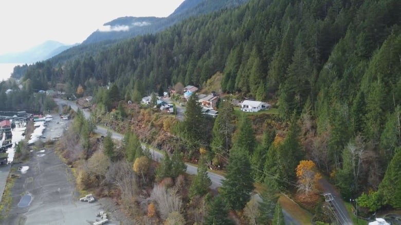 tahsis-drone-shot A drone shot of a small row of houses at the base of lush green trees on the side of a mountain.