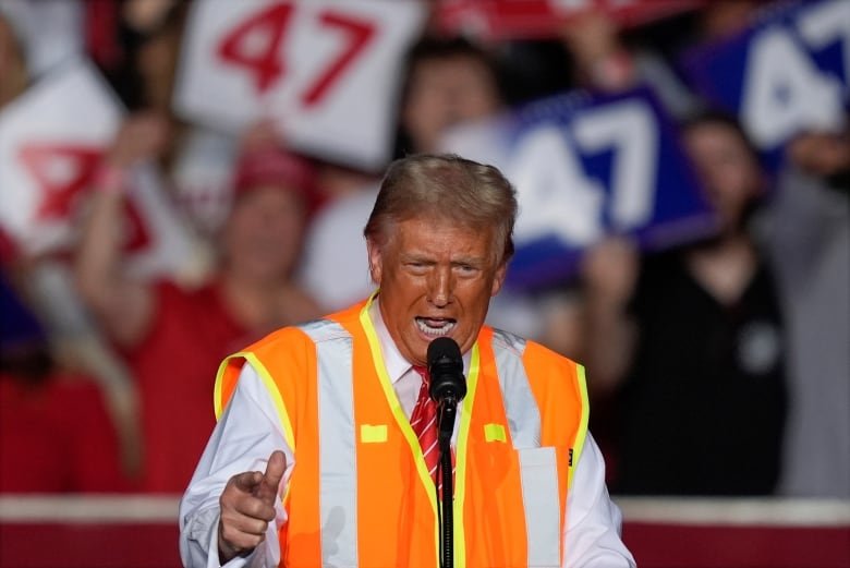 A man in an orange high-vis vest appears on stage at a political rally.