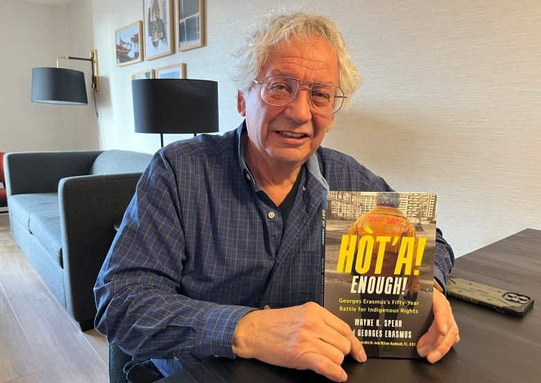 A man sits at a table holding up a book.