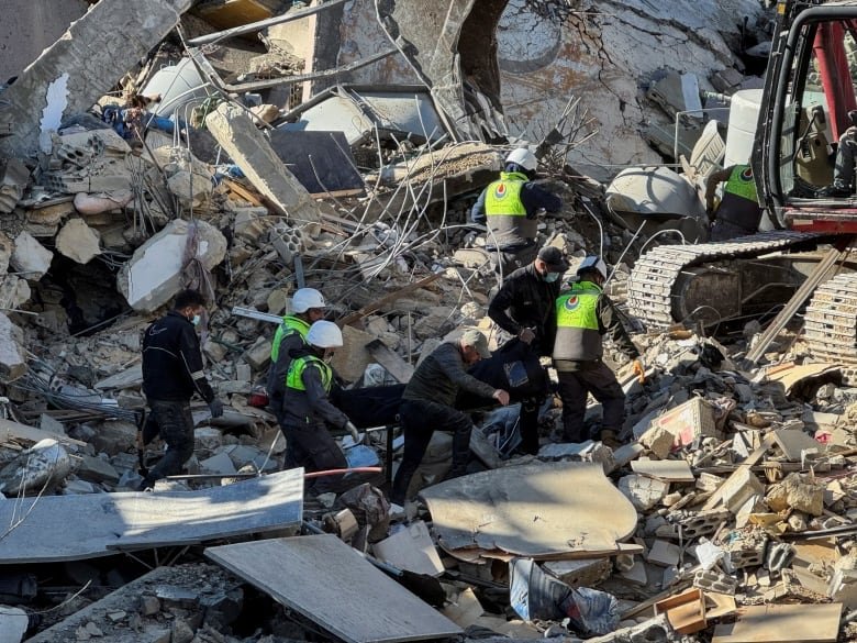 People carry a body as they walk on rubble of damaged buildings.