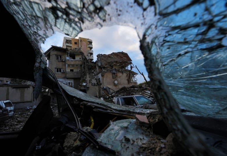 Damaged building pictured through wreckage of a vehicle.