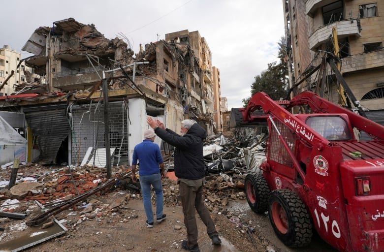 Two men walk through damaged site.