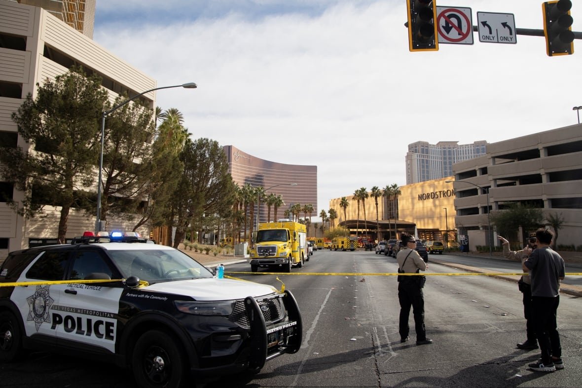 tesla-cybertruck-fire-2 Law enforcement officers stand behind yellow tape in a cordoned area.
