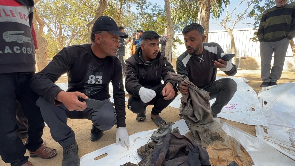 families-search-for-loved-ones-gaza Three men sit in front of white body bags.