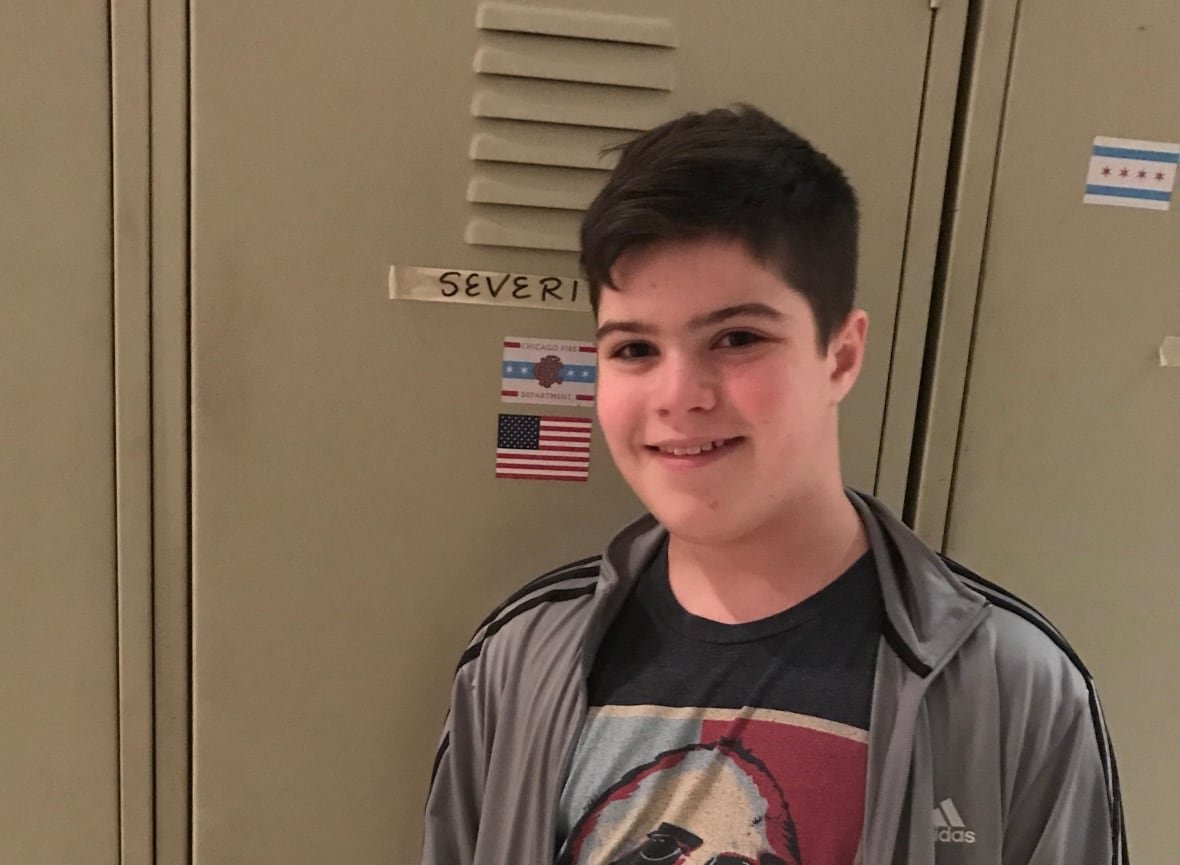 sammy-chapman A teenage boy with short, dark hair smiles while standing in front of a school locker.