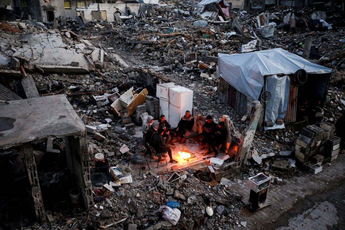 israel-palestinians-gaza-ceasefire-aid-1 People gather near a fire next to the rubble of destroyed buildings.