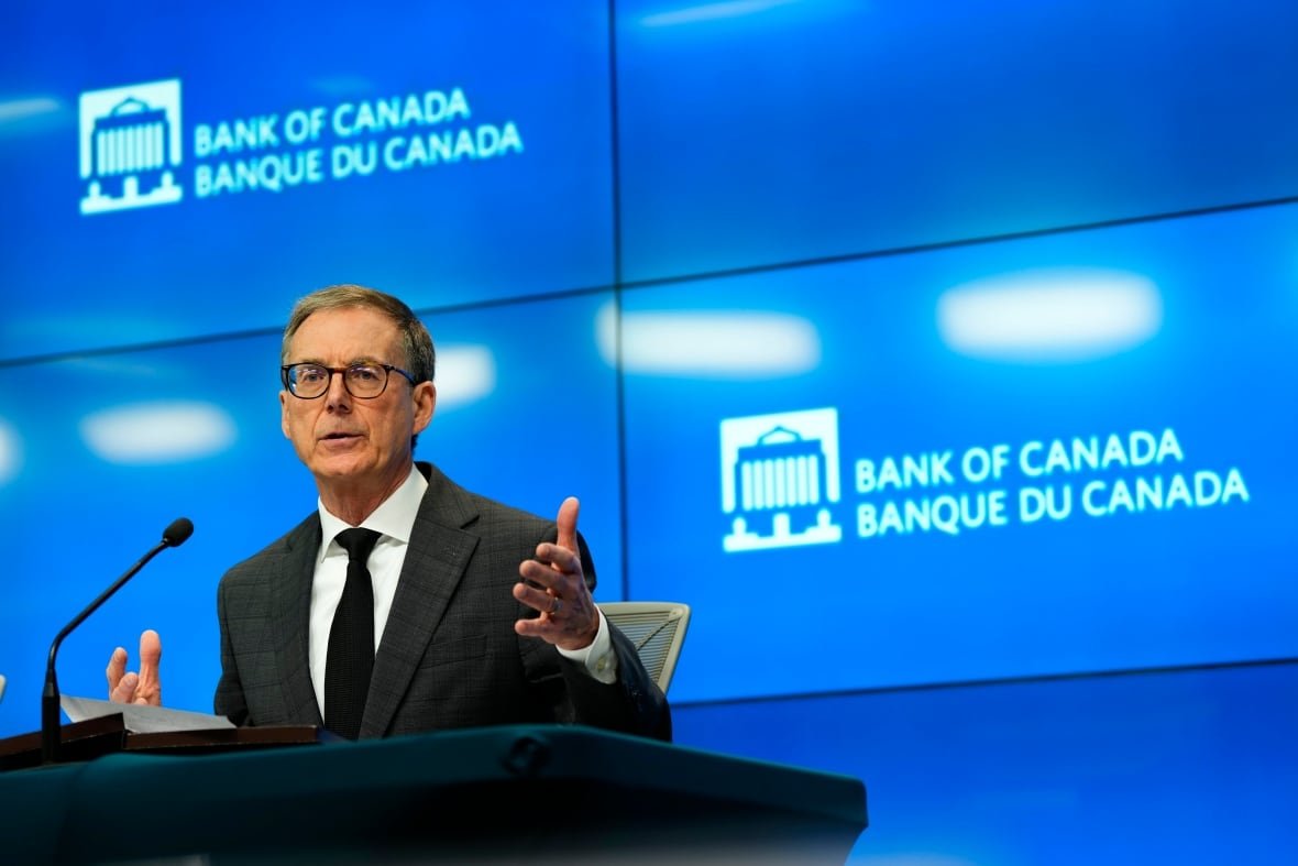 boc-interest-rate-20250416 a man in a suit and glasses sits at a desk answering questions. behind him is a blue background that says "Bank of Canada"