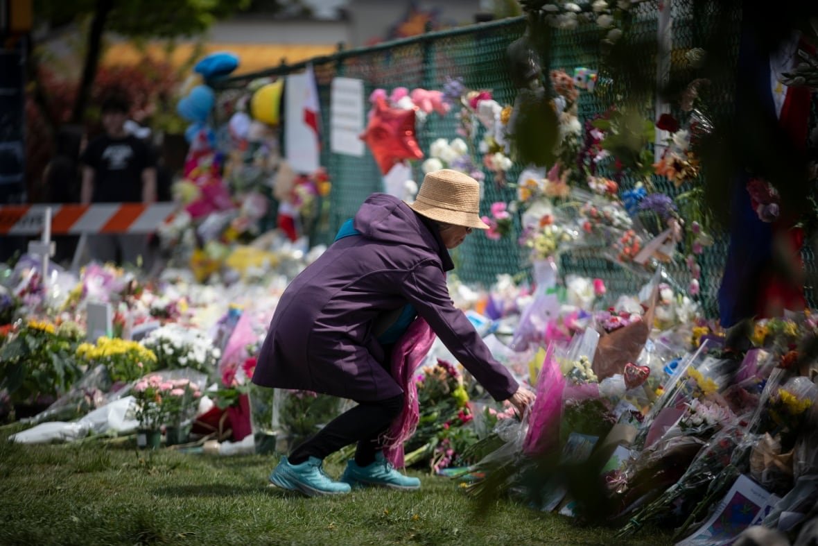 lapu-lapu A woman in a purple hooded jacket, blue sneakers and a straw hat lays flowers at a memorial along a fence.