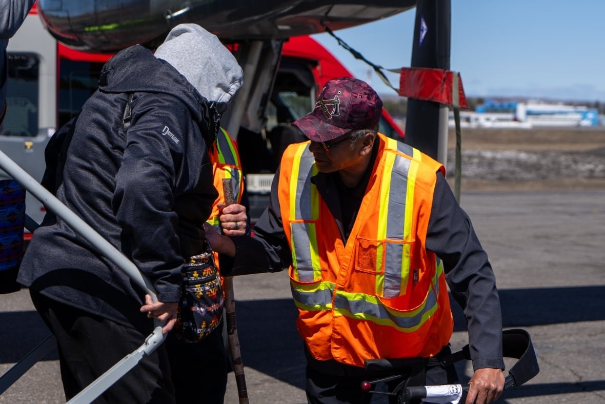 neskantaga-first-nation-chief-gary-quisess-1 A man wearing a safety vest helps a woman with a cane off a plane.