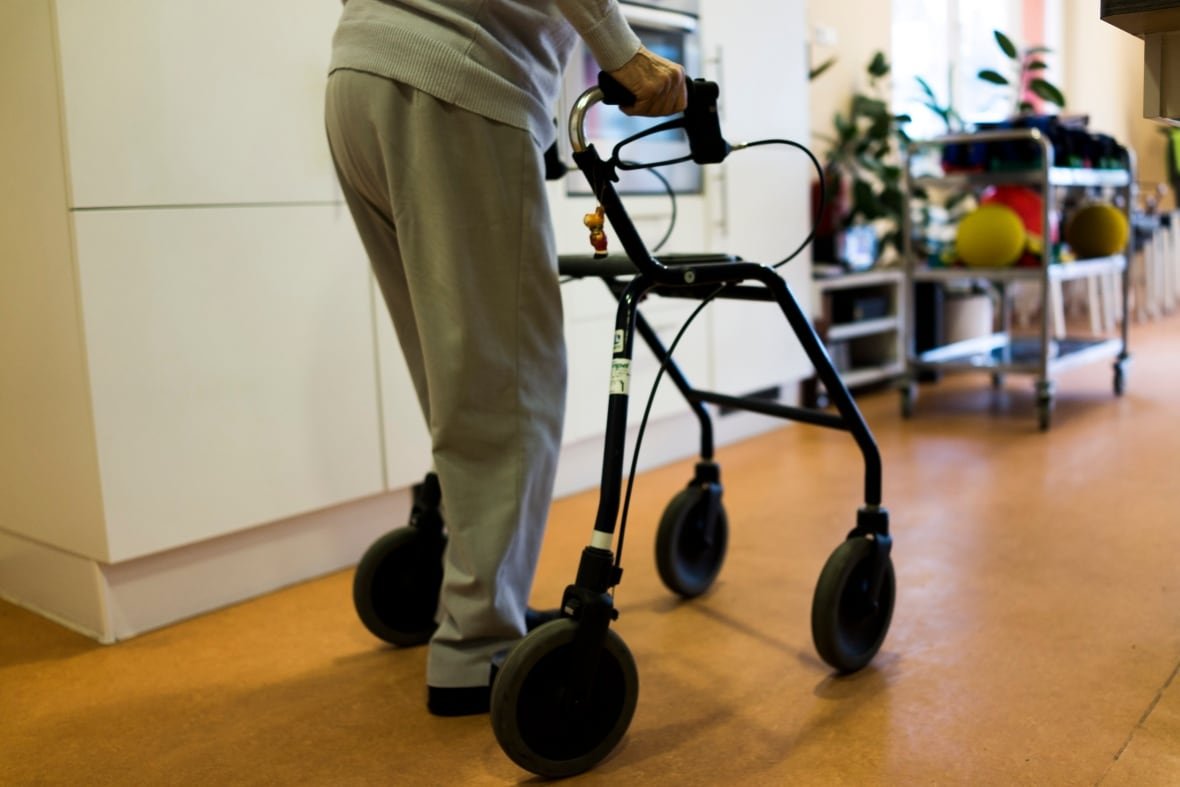 164124283-1 A person with only hands and legs visible using a walker on a wood floor.