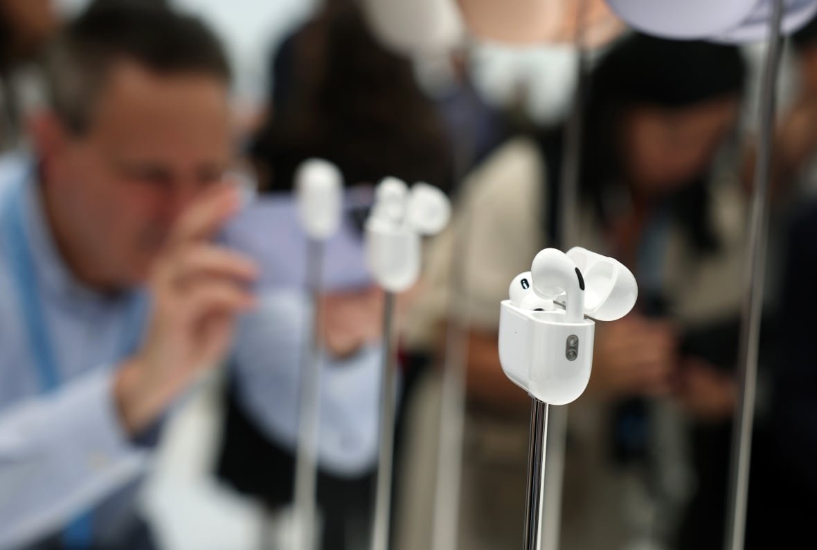 2171047190-apple-airpods White coloured Apple earbuds are seen at a press event. A man is seen in the background staring at them.
