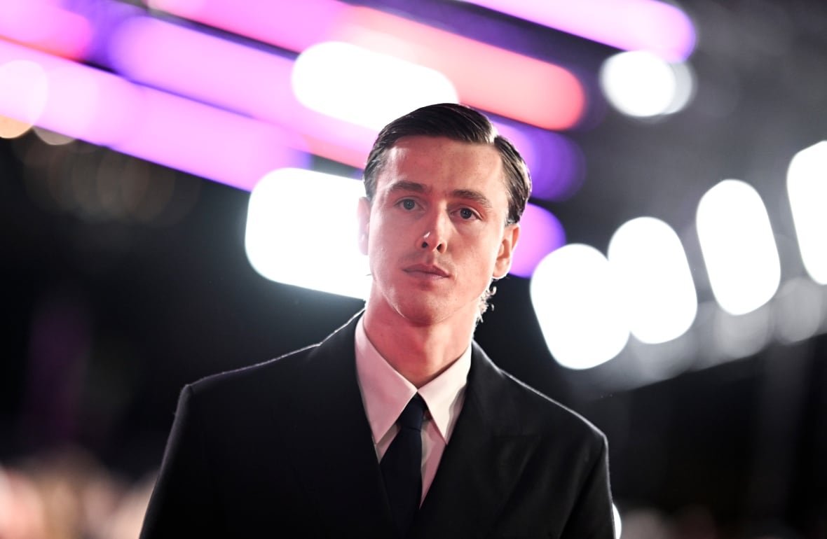2177658370 A young man with a light bear wearing a suit and tie is shown surrounded by bright lights.