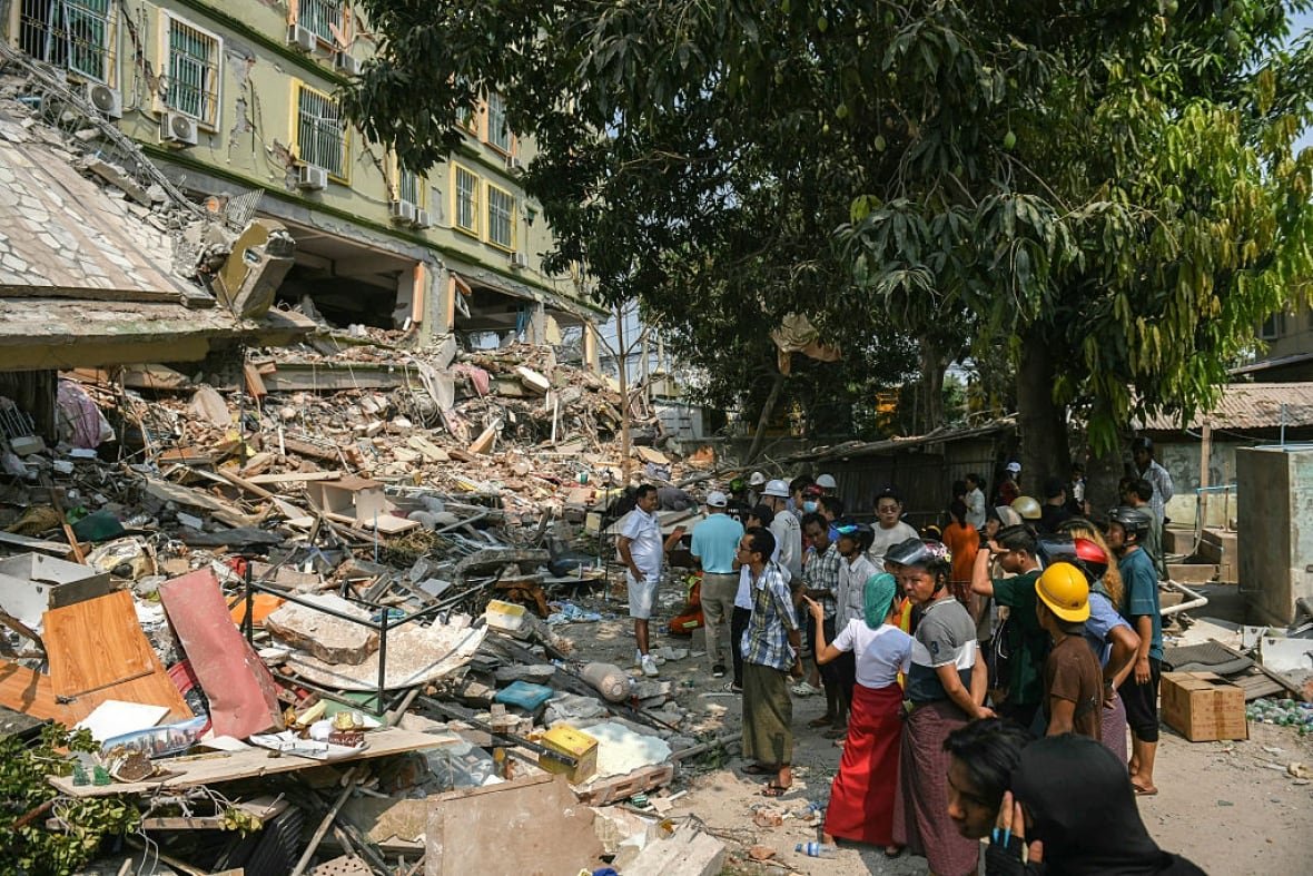 2206825823 People gather near a building destroyed by an earthquake.