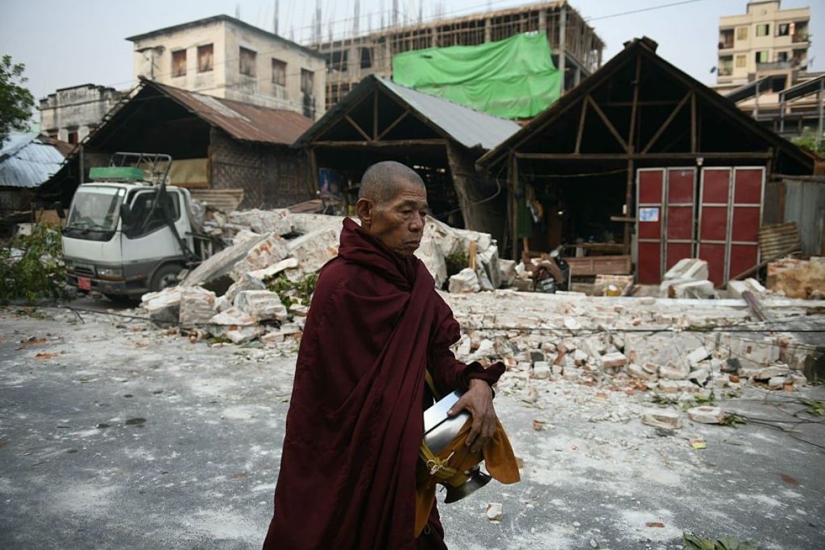2207003465 A monk in a robe walks near earthquake damage.