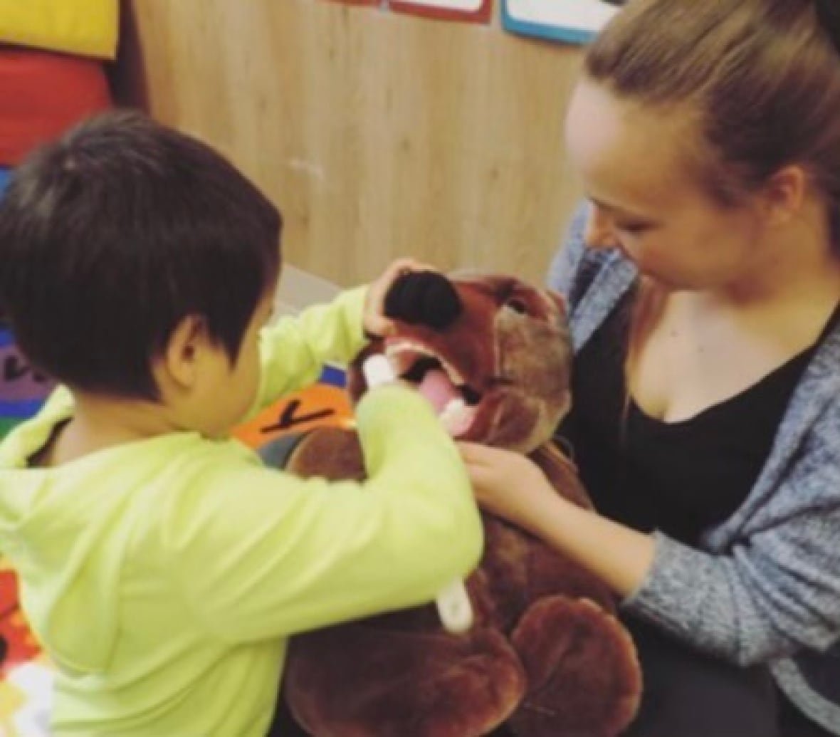 camille-poirier-4 A woman showing a child how to brush teeth with a teddy bear.