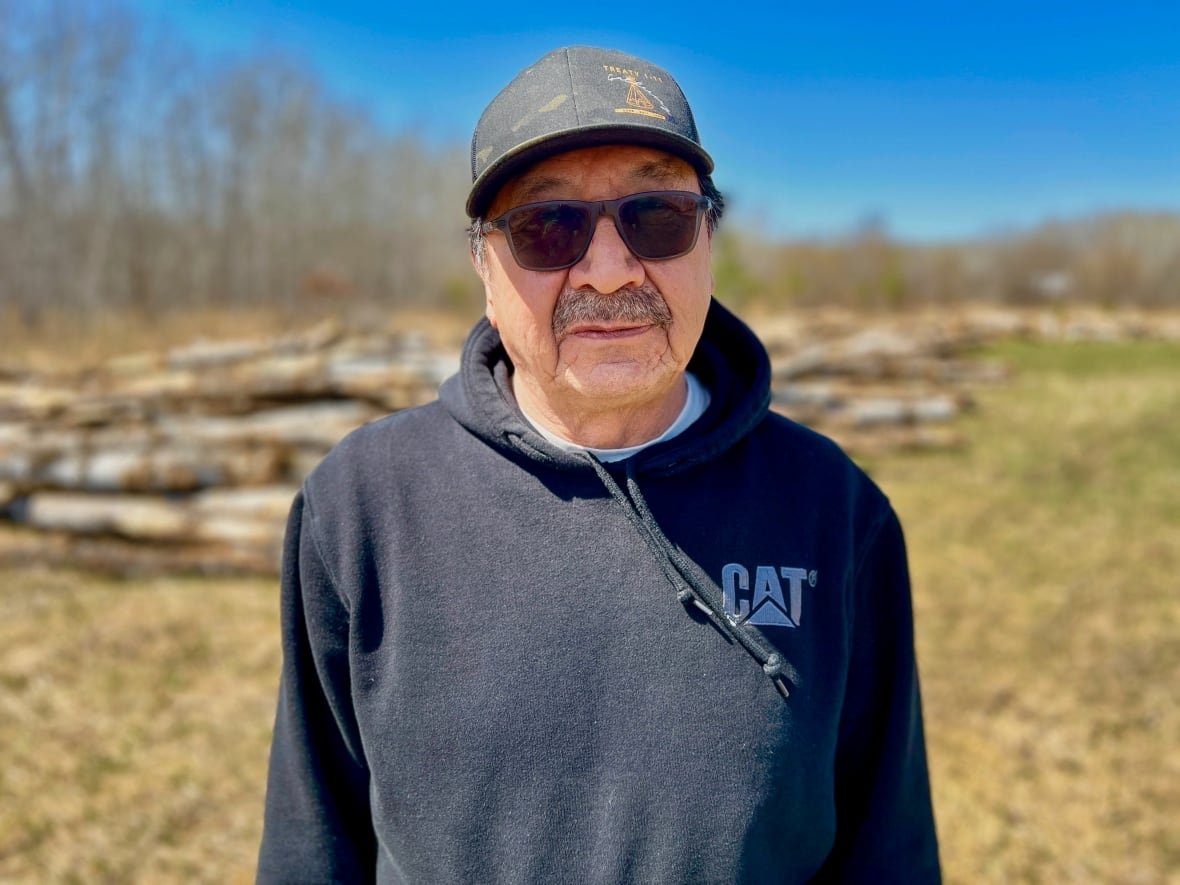 carl-smith-brokenhead-ojibway-nation A older man stands in front of some tree logs.