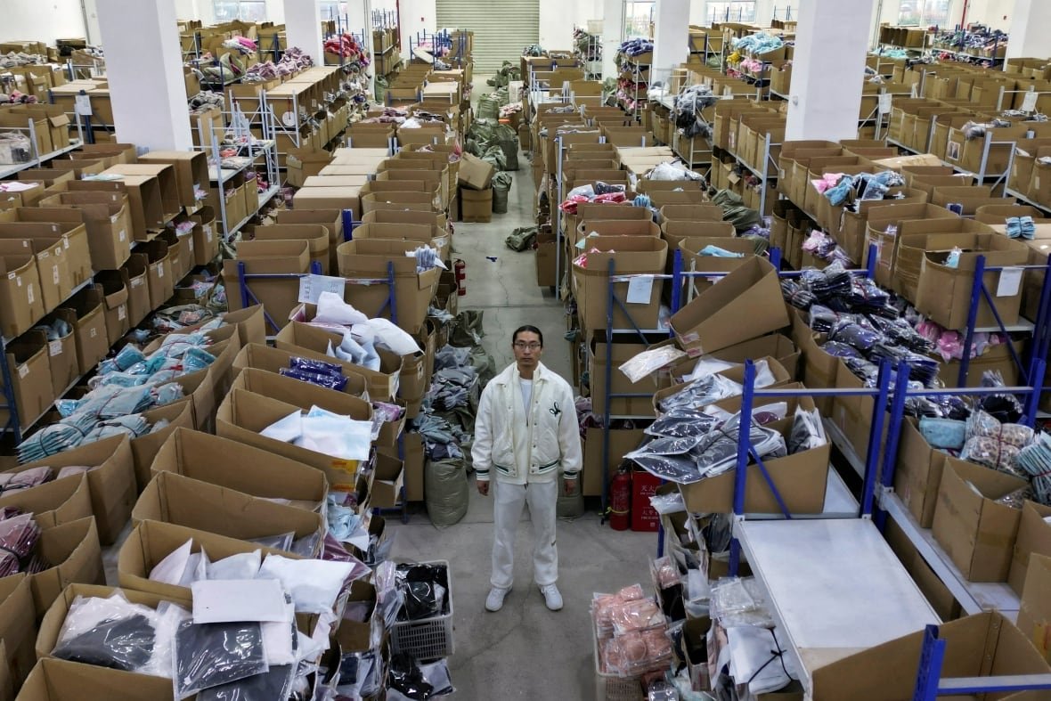 china-usa-trade-de-minimis Rows and rows of boxes are shown from an elevated view in a factory, with a man looking at the direction of the camera.