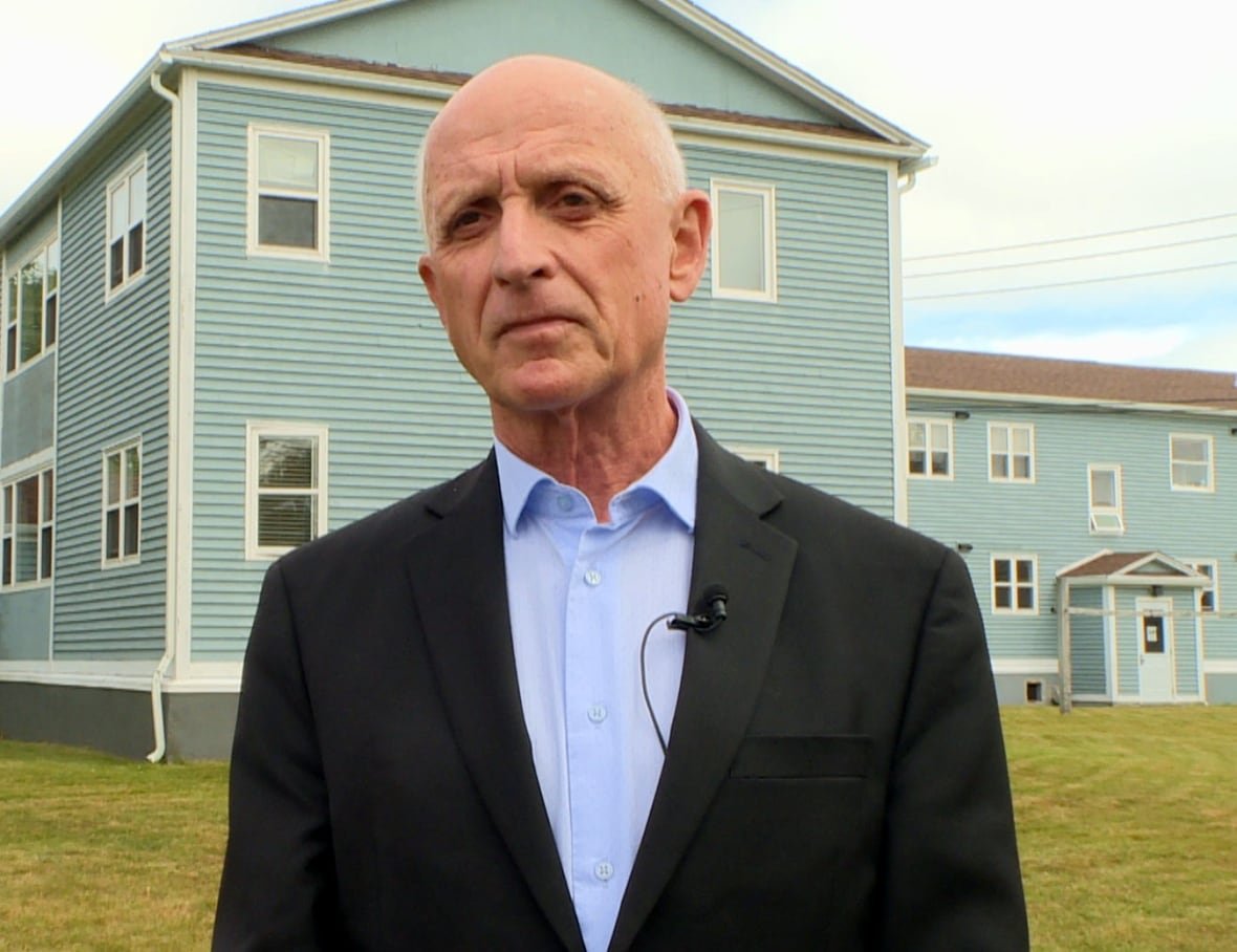 dennis-browne A person wearing a blue shirt and black blazer stands outside on a lawn.