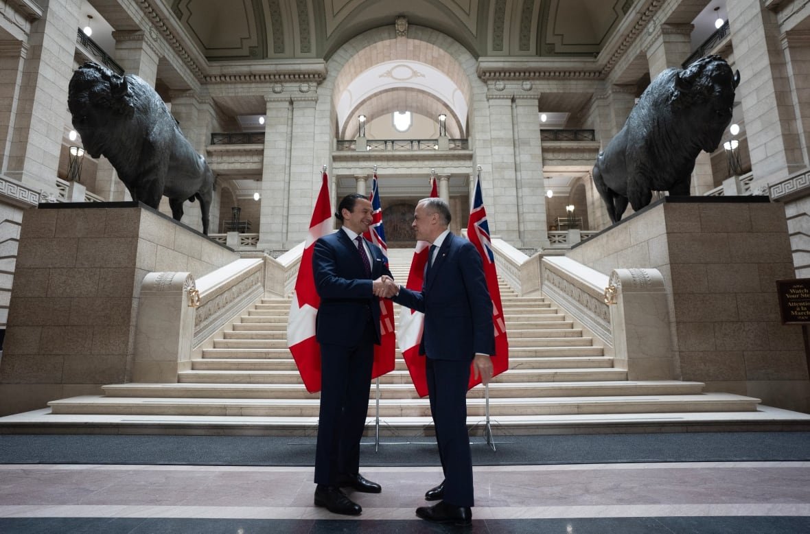 fedelxn-liberals-20250401-2 Two men shake hands in front of flags in a legislature lobby.