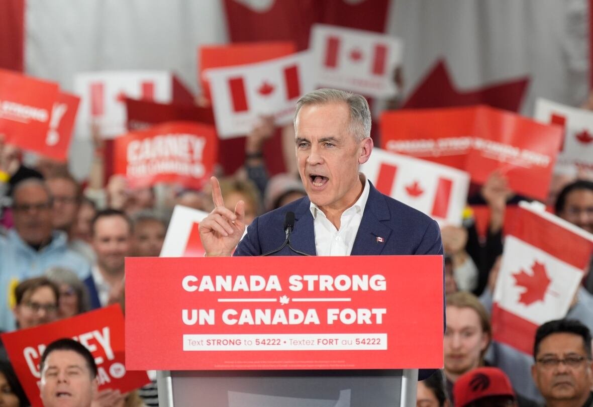 fedelxn-liberals-20250401-4 A man stands at a podium with the words "Canada Strong" and dozens of people holding signs with Canadian flags behind him.