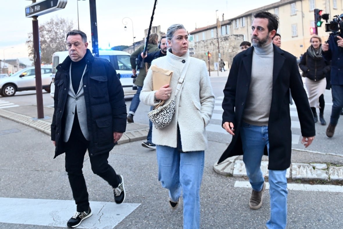 france-justice A woman and two men are followed by a cameraperson as they walk down a street.