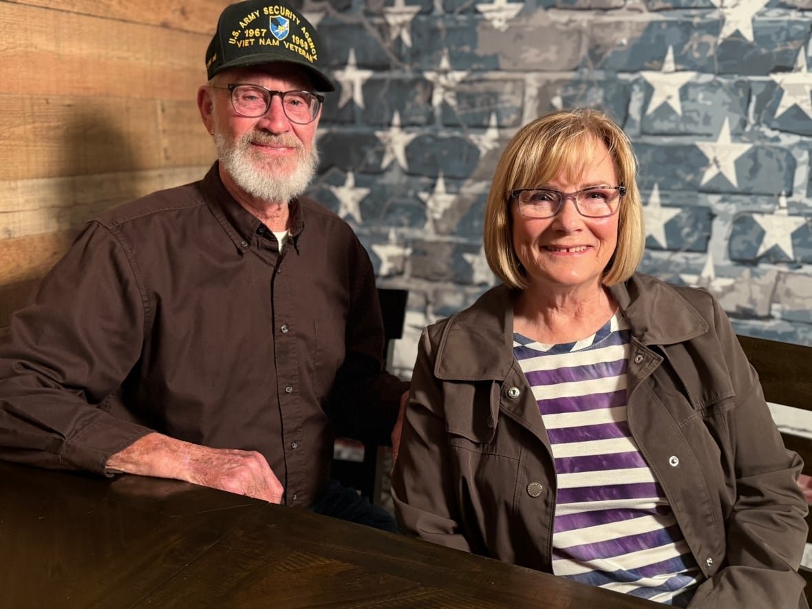 gale-and-ginny-delano A man and a woman sit in front of a brick wall painted blue with white stars.