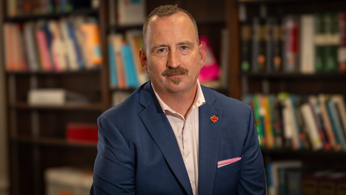 Headshot of man in suit with books in the background.
