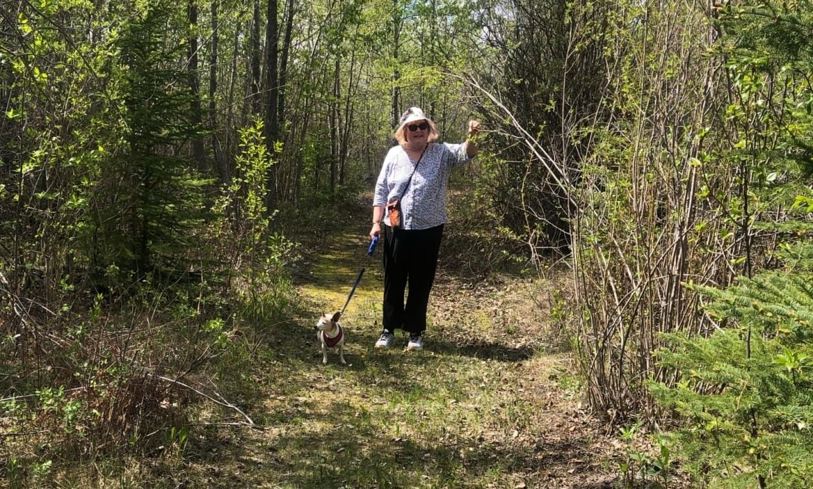 gerri-kunneke-at-gooseberry-park Woman wearing sunglasses and a hat walking a dog on a path surrounded by trees.