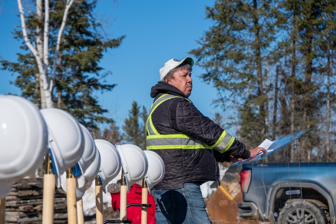 grassy-narrows-mercury-care-home A person wearing a high-vis vest stands at a podium ourside, next to a row of shovels and white hard hats.