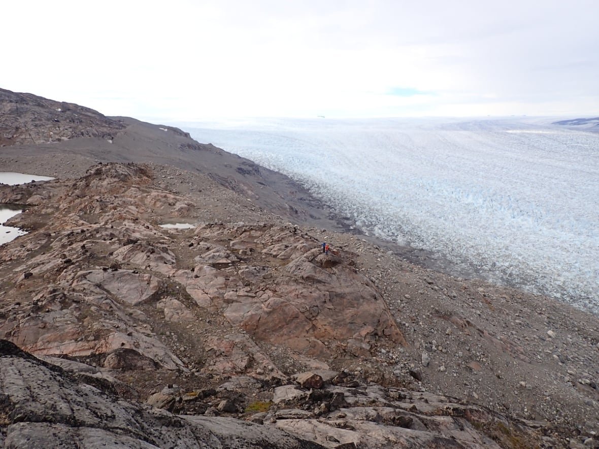 human-scale-ice-in-greenland This is a scene of a rocky landscape with glacial ice in Greenland. Two human subjects are dwarfed by the immensity of it.