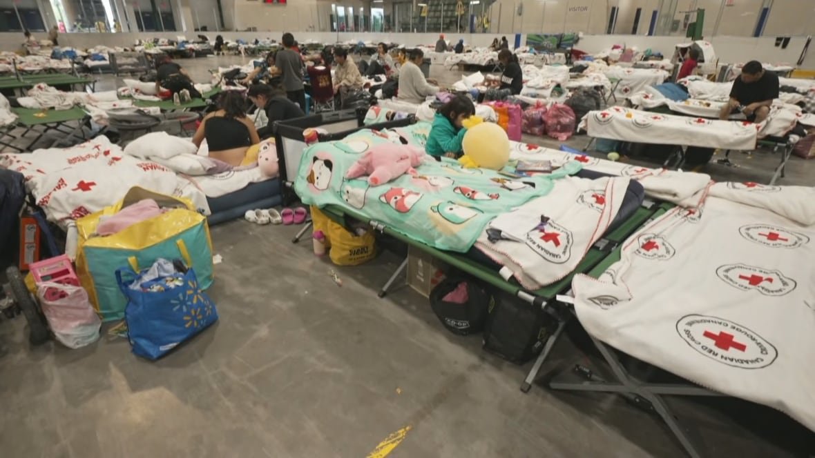 inside-thompson-evacuation-centre-june-3-2025 People sit on cots lined up in rows inside an arena.