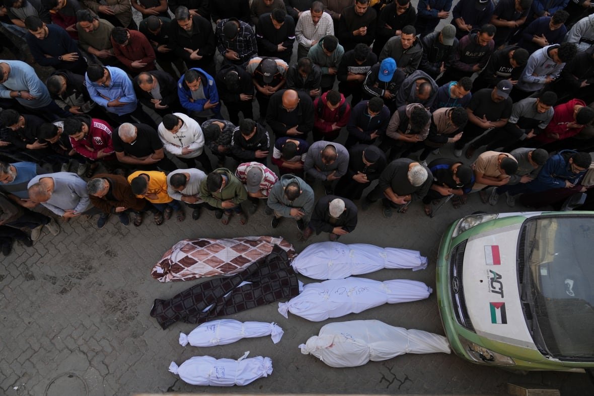 israel-palestinians-2 People pray over seven bodies in white shroud.
