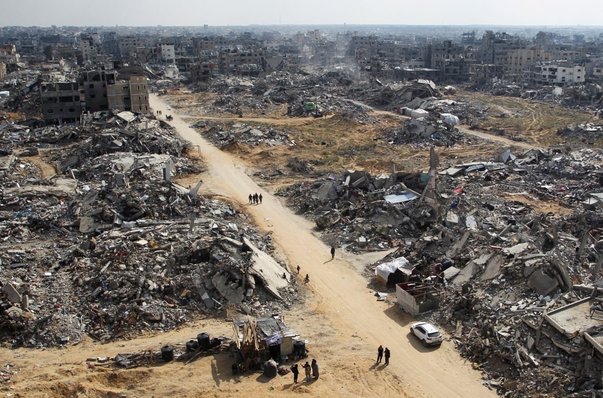 israel-palestinians-gaza-ceasefire An aerial view shows a city block completely destroyed as people walk on a dirty road that runs through it.