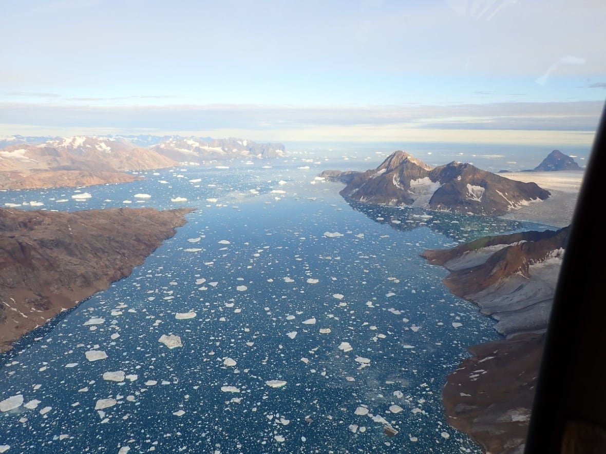 kangerlussuaq-fjord-outlet-in-greenland An aerial shot of icebergs floating in a fiord surrounded by mountains in Greenland.