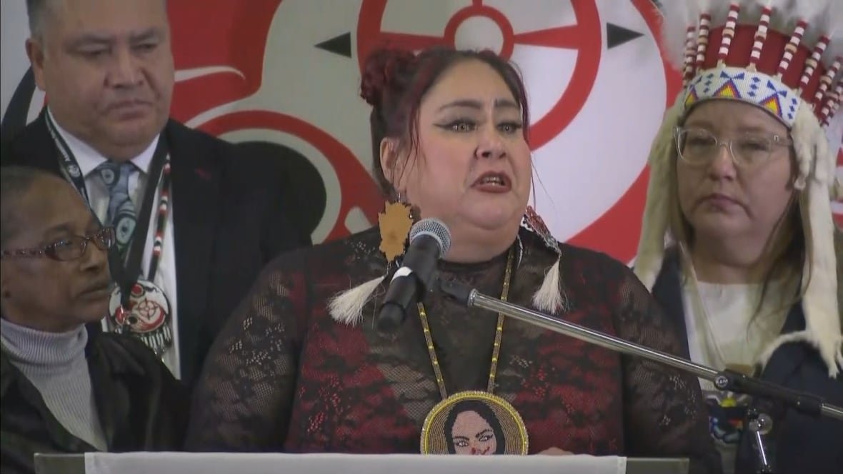 A woman stands in front of two people at a microphone while she speaks.