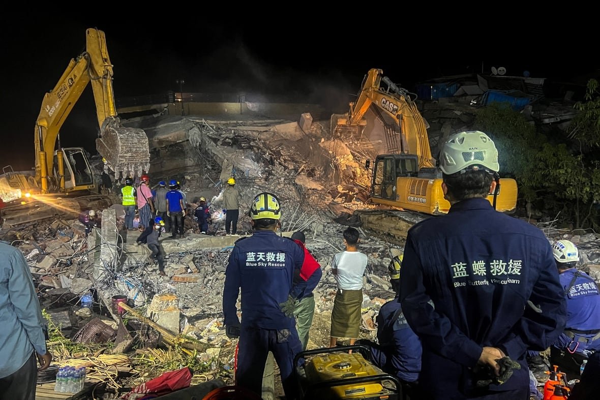 myanmar-quake-4 People stand in front of collapsed building rubble