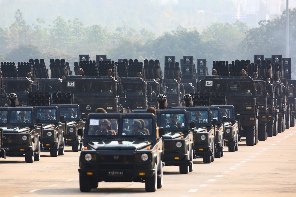 myanmar-us-sanctions A line of military jeeps parade down a road.