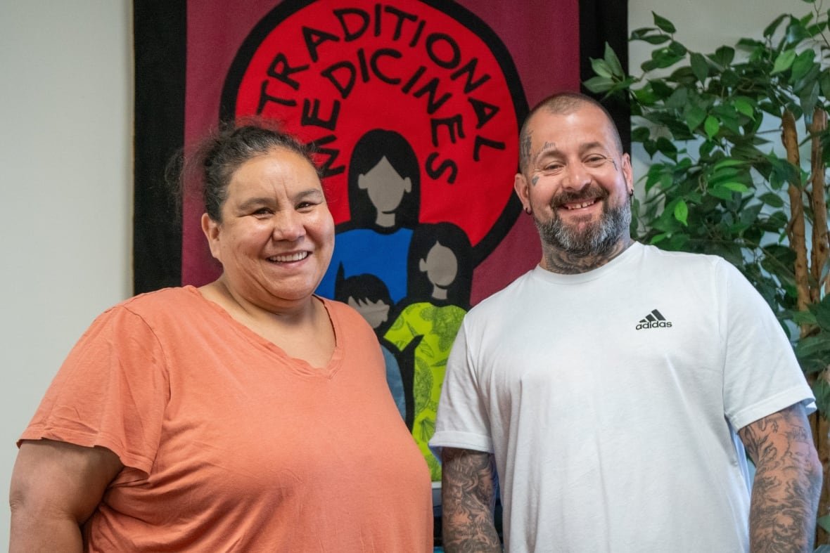 Two people stand together in front of a banner that says "Traditional Medicines."