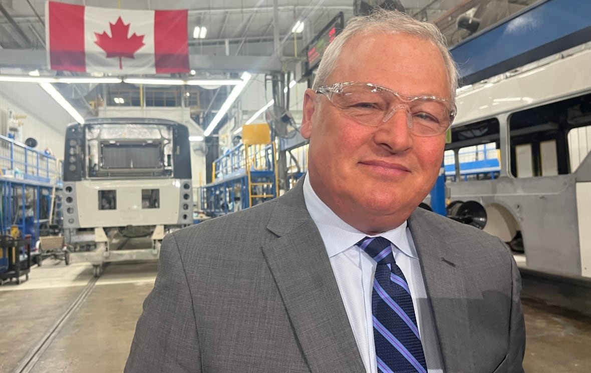 paul-soubry-nfi-april-1-2025 A man in a suit standing in front of buses and a Canadian flag.